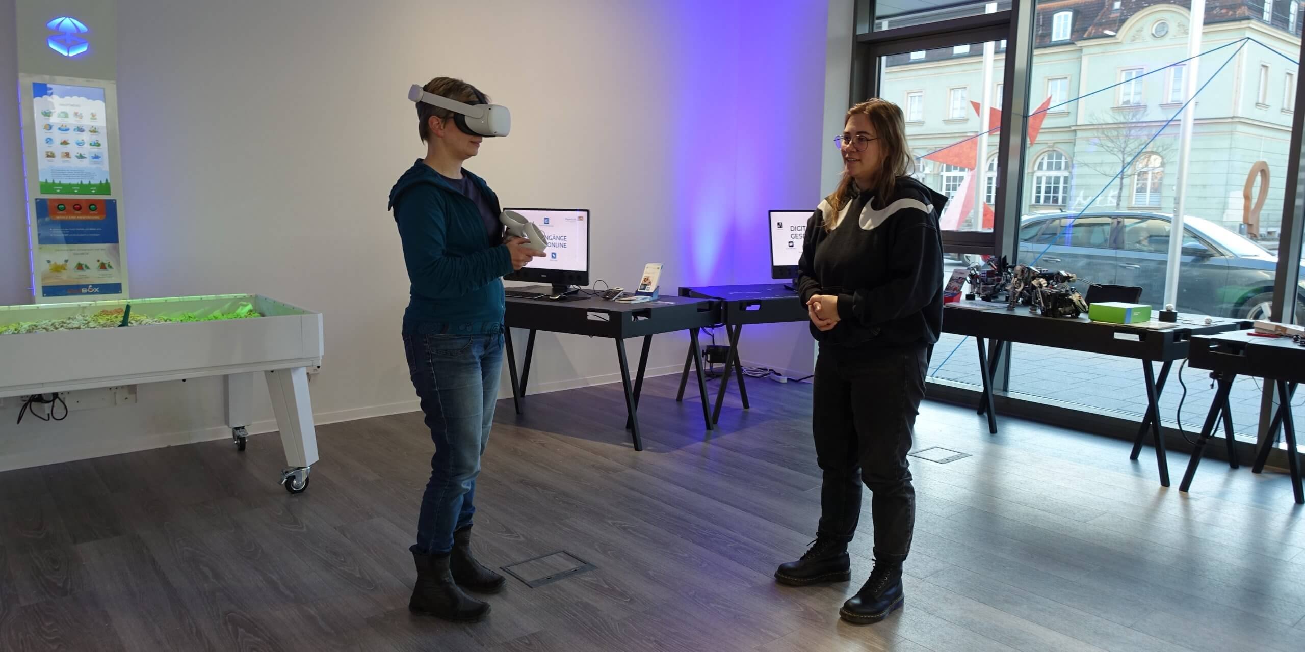 Infoveranstaltung BayernLab Eine Frau trägt eine VR-Brille. Eine andere Frau steht daneben und sieht zu.