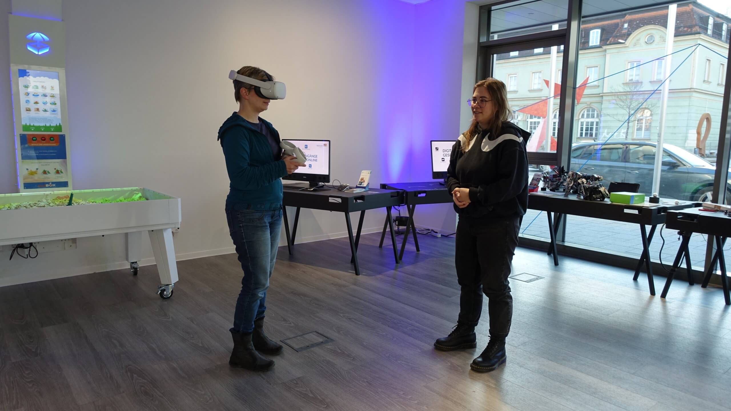 Infoveranstaltung BayernLab Eine Frau trägt eine VR-Brille. Eine andere Frau steht daneben und sieht zu.